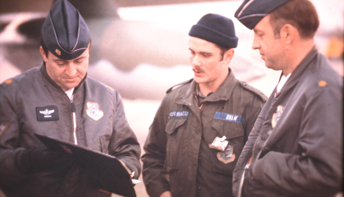 three men in cold weather uniforms talking and looking at binder