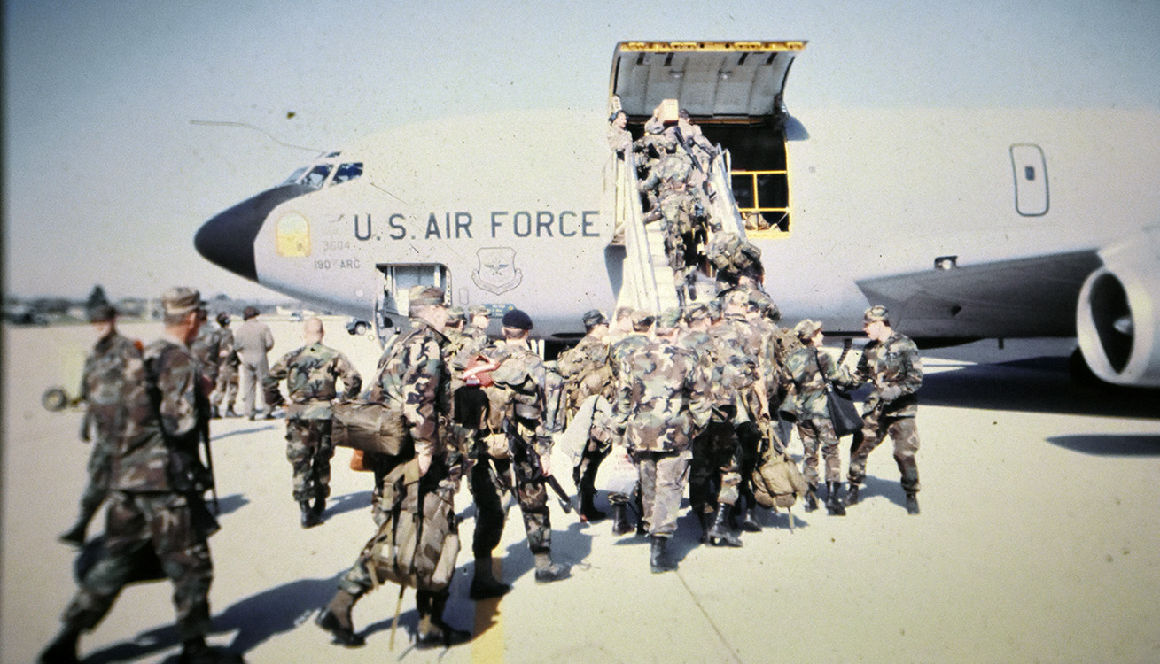 multiple service members carrying their bags to an aircraft and walking up the stairs.