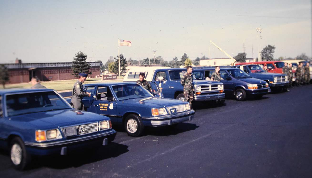 multiple cars lined up with service members standing outside of them.